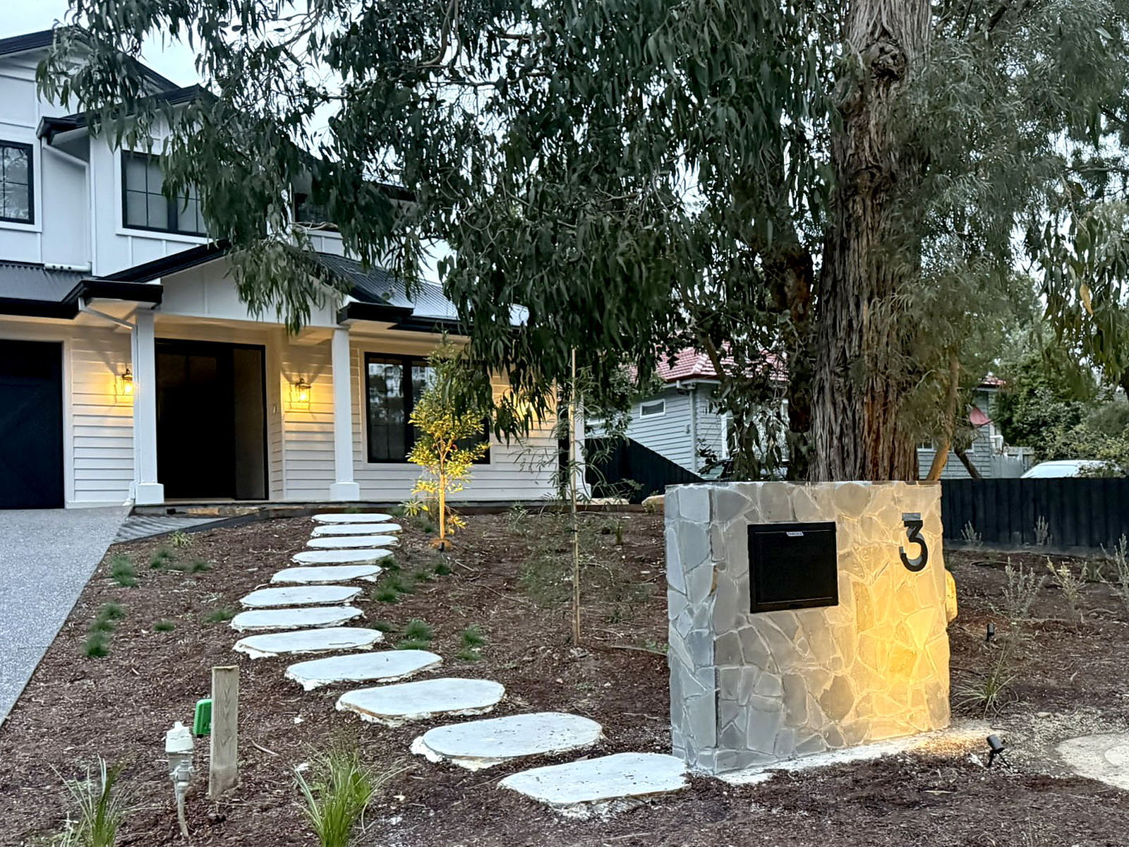 The crazy-paved bluestone postbox and stepping stone path at dusk, with the Forest Hill house lit behind